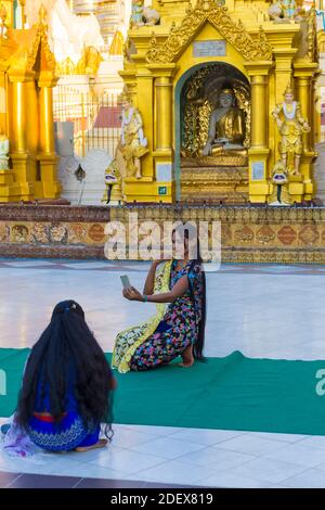 Hübsche junge Besucherin mit sehr langen schwarzen, geraden Haaren, die im Februar Selfie in der Shwedagon Pagode, Yangon, Myanmar (Burma), Asien machen Stockfoto