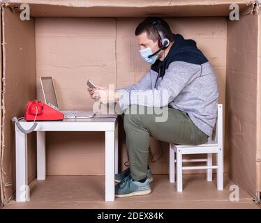 Der Mitarbeiter arbeitet aus seinem eigenen Kartonbüro, um sich zu isolieren Von anderen Stockfoto