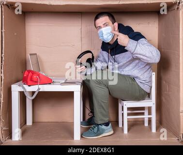 Der Mitarbeiter arbeitet aus seinem eigenen Kartonbüro, um sich zu isolieren Von anderen Stockfoto