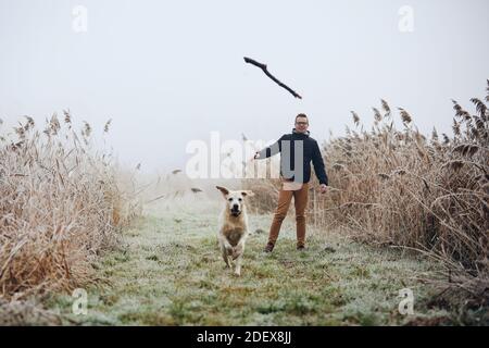 Mann wirft Stock für seinen Hund. Haustierbesitzer mit labrador Retriver spielen während des nebligen Herbsttages. Stockfoto