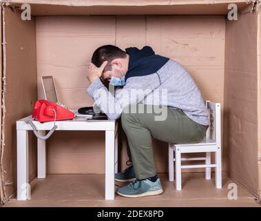 Der Mitarbeiter arbeitet aus seinem eigenen Kartonbüro, um sich zu isolieren Von anderen Stockfoto