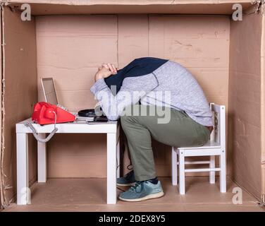 Der Mitarbeiter arbeitet aus seinem eigenen Kartonbüro, um sich zu isolieren Von anderen Stockfoto