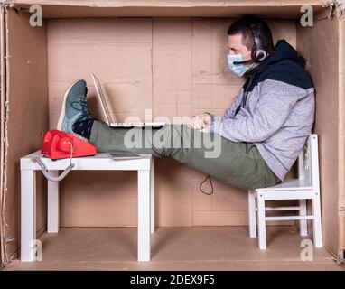 Der Mitarbeiter arbeitet aus seinem eigenen Kartonbüro, um sich zu isolieren Von anderen Stockfoto