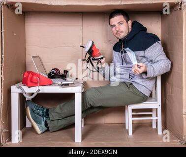 Der Mitarbeiter arbeitet aus seinem eigenen Kartonbüro, um sich zu isolieren Von anderen Stockfoto