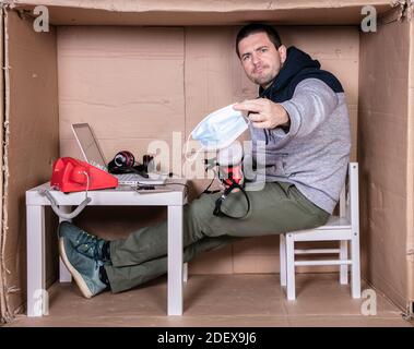 Der Mitarbeiter arbeitet aus seinem eigenen Kartonbüro, um sich zu isolieren Von anderen Stockfoto