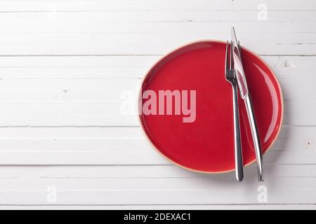 Roter Vintage Teller mit Besteck auf weißem Hintergrund, Draufsicht, Freiraum Stockfoto