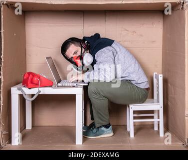 Der Mitarbeiter arbeitet aus seinem eigenen Kartonbüro, um sich zu isolieren Von anderen Stockfoto
