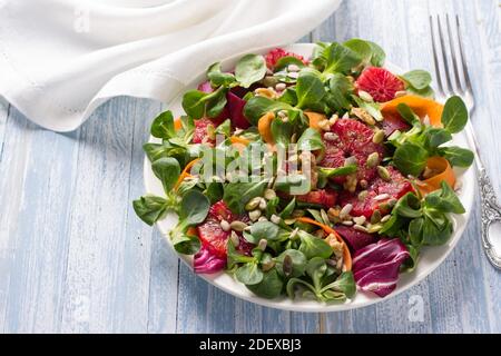 Grüner Salat mit Blutorangen, Karotten, Rüben, Samen und Nüssen auf hellblauem Hintergrund, freier Platz. Leckere gesunde Lebensmittel Stockfoto