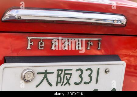 Detailansicht des Ferrari-Namensabzeichens und des Nummernschilds auf der Rückseite eines roten Sportwagens des Dino 246 GT aus den 1970er Jahren. Japanische Schrift liest Osaka. Stockfoto