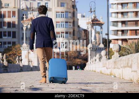 Ein nicht erkennbarer junger Mann reist während einer Pandemie mit einem blauen Koffer nach Spanien, während er zu Arbeitszwecken durch das Zentrum einer Stadt geht. Busi Stockfoto