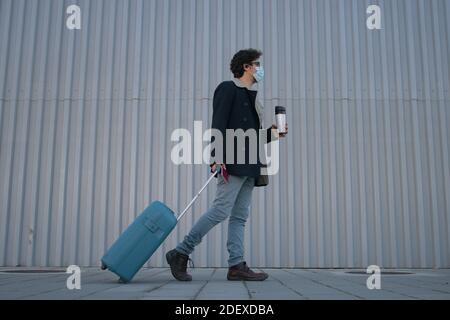 Mann mit Koffer und Reisepass in der Hand. Er geht direkt zum Flughafen mit einem Kaffee zum Mitnehmen während Covid 19. Stockfoto