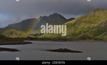 Schöne Aussicht auf die südöstliche Küste der Insel Vestvågøy, Lofoten, Norwegen mit Felsen im Wasser, schroffen Bergen und schönen starken Regenbogen. Stockfoto