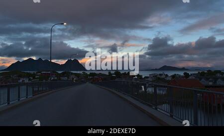 Schöne Aussicht auf Fischerdorf Svolvaer mit typischen roten Holzhäusern auf Austvågøya, Lofoten, Norwegen von der Brücke am Abend mit orangen Wolken. Stockfoto