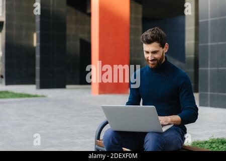Glücklicher Mann, der vor seinem Büro am Laptop arbeitet Stockfoto