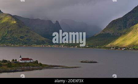 Schöne Aussicht auf Sildpollnes Kirche auf einer Halbinsel in einem Fjord auf Austvågøy Insel, Lofoten, Norwegen mit Dorf und Sonne scheint auf Bergen. Stockfoto