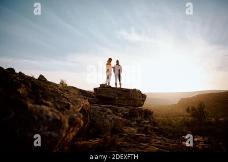 Rückansicht des jungen Paares, auf dem Freunde stehen Klippenrand mit Blick auf den wunderschönen Sonnenaufgang Stockfoto