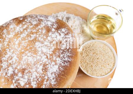 Weißes Rundbrot mit Sesam und Zutaten auf Holzplatte, auf weißem Hintergrund. Stockfoto