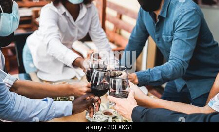 Junge, multirassische Menschen jubeln mit Wein, während sie Schutzmasken tragen - Social Abstand Konzept - Fokus auf unteren weißen Hand Stockfoto
