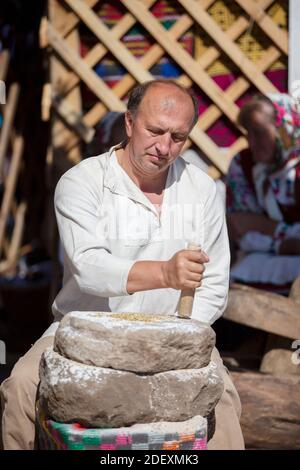 29. August 2020. Weißrussland, das Dorf Ljaskowitschi. Ein Urlaub des alten Handwerks. Ein Mann mahlt Mehl auf alte Weise mit Hilfe von Steinmühlen. Stockfoto