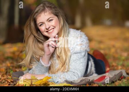 Schöne junge blonde Frau liegt auf gelben Blättern im Herbstpark. Mädchen im Herbst. Stockfoto