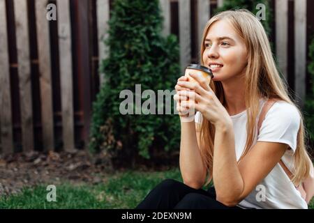 Porträt eines jungen Mannes in einem weißen T-Shirt, im Freien mit einer Tasse Kaffee. Mädchen auf dem Rasen sitzen und Kaffee trinken. Stockfoto