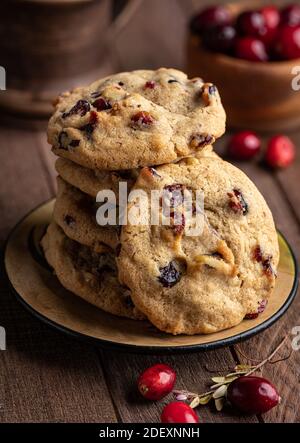 Cranberry Walnuss Cookies auf einem Teller mit Schüssel gestapelt Preiselbeeren im Hintergrund auf rustikalem Holztisch Stockfoto