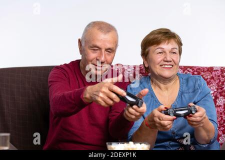 Seniorenpaar spielt zu Hause, sitzt auf der Couch ein Videospiel. Konzeptzeit während der Quarantäne. Stockfoto