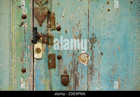 Alte Holztür, in Teal (blau grünlich) Farbe lackiert. Von Zeit und Wetter beschädigt. Mit vielen verrosteten Schlüssellöchern und verriegelt. Französische Landschaft. Stockfoto