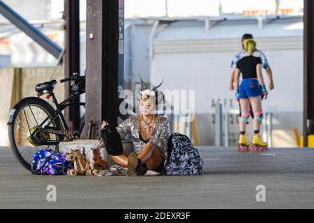 NEW ORLEANS, LA - 15. NOVEMBER 2020: Kostümierte Rollerskaterin, die ihre Rollerskates mit einem Paar Skater im Hintergrund im Crescent Park aufsetzt Stockfoto