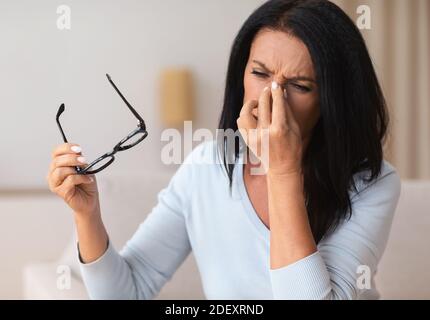 Müde reife Frau massiert Nasenbrücke zu Hause Stockfoto
