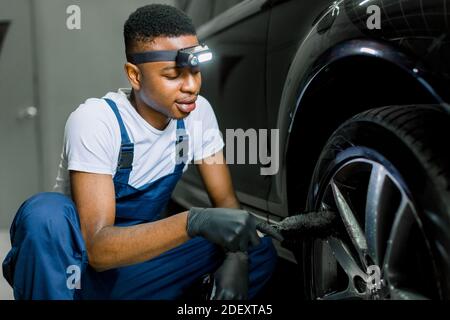 Autowäsche und Detaillierung Werkstatt. Afrikanischer Mann Arbeiter in schützenden Overalls und Gummihandschuhe, waschen Auto-Legierung Rad auf einer Autowäsche, mit speziellen Stockfoto