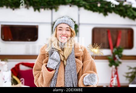 Fröhliche blonde Dame posiert mit Sparkler im Freien in der Nähe Wohnmobil an Wintercampingplatz Stockfoto