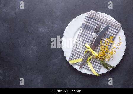 Ostertisch. Weißer Teller, Mimosenblumen und Besteck auf Steingrund. Draufsicht Stockfoto