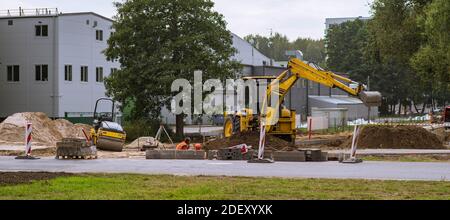 Straßenbauarbeiten. Gelber Bagger und Straßenwalze. Straßenreparaturarbeiten. Ausgegrabener Sand. Stockfoto