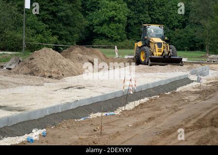Baustelle des Bürgersteiges in der Stadt. Gelber Traktor. Haufen von ausgegrabenen Boden. Neue Betonkanten. Stockfoto