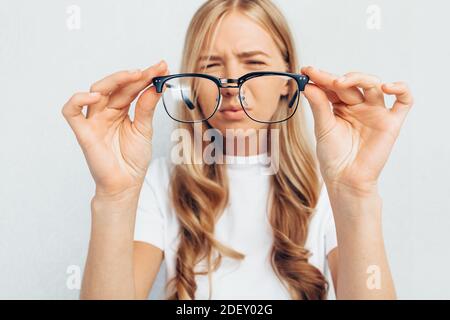 Junges Mädchen in weißem T-Shirt, Brille haltend, selektiver Fokus auf Brille, auf grauem Hintergrund stehend, Konzept: Schlechtes Sehvermögen Stockfoto