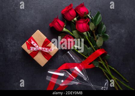 Rote Rose Blumen Bouquet, Geschenkbox, Champagner Gläser auf schwarzem Stein Hintergrund Valentinstag Grußkarte Copy space Draufsicht Stockfoto