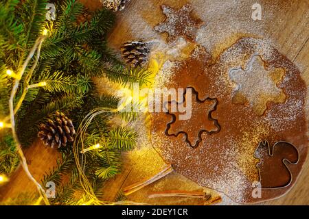 Gerollter Teig für Lebkuchen auf einem Hintergrund aus Schlamm und Girlanden. Weihnachtsplätzchen machen. Layout des neuen Jahres. Blick von oben Stockfoto