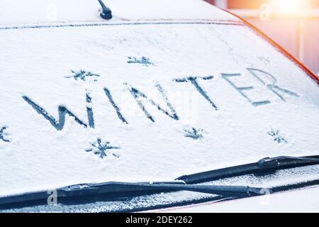 Word Winter mit Finger auf einer schneebedeckten Windschutzscheibe geschrieben Ein Auto Stockfoto