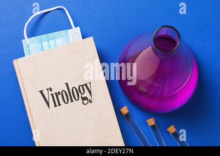 Virologisches Lehrbuch mit einem Lesezeichen aus einer medizinischen Maske und verschiedenen Reagenzien auf dem Tisch. Stockfoto