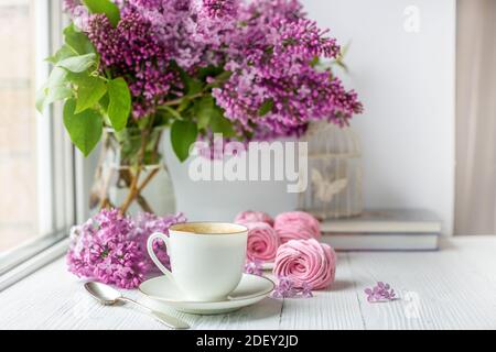 Bouquet von Flieder, Tasse Kaffee, hausgemachte Marshmallow und Stapel von Büchern. Romantischer Frühlingsmorgen. Selektiver Fokus Stockfoto