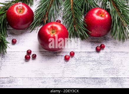 Weihnachtlicher Hintergrund mit Ästen, roten Äpfeln und Preiselbeeren. Heller Holztisch. Draufsicht. Speicherplatz kopieren Stockfoto