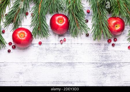 Weihnachtlicher Hintergrund mit Ästen, roten Äpfeln und Preiselbeeren. Heller Holztisch. Draufsicht. Speicherplatz kopieren Stockfoto