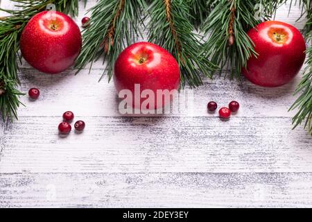 Weihnachtlicher Hintergrund mit Ästen, roten Äpfeln und Preiselbeeren. Heller Holztisch. Draufsicht. Speicherplatz kopieren Stockfoto