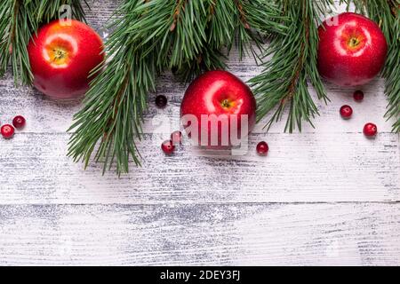 Weihnachtlicher Hintergrund mit Ästen, roten Äpfeln und Preiselbeeren. Heller Holztisch. Draufsicht. Speicherplatz kopieren Stockfoto