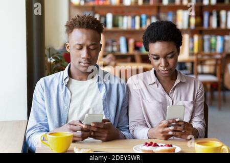 Gadget sucht und Phubbing. Junge schwarze Paar mit stumpfen Datum, stecken in Smartphones, ignorieren einander im Café Stockfoto