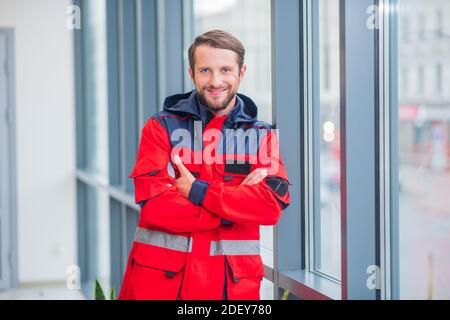 Bärtiger Arzt in roter Uniform, der neben dem Fenster steht Stockfoto