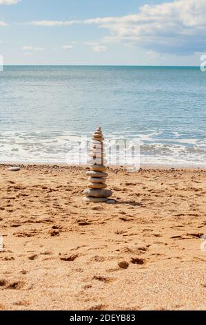 Gestapelte Zen-Steine am Sandstrand mit ruhigem Meerwasser im Hintergrund. Stockfoto