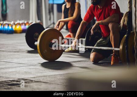 Stock Foto von zwei Menschen kniend vor den Langhanteln. Sie sind nicht erkennbar. Sie tragen Sportkleidung. Stockfoto