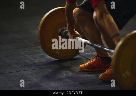 Stock Foto von einem erwachsenen Mann in einer Turnhalle hocken und Heben einer Langhantel. Er ist nicht erkennbar. Er trägt Sportkleidung. Stockfoto